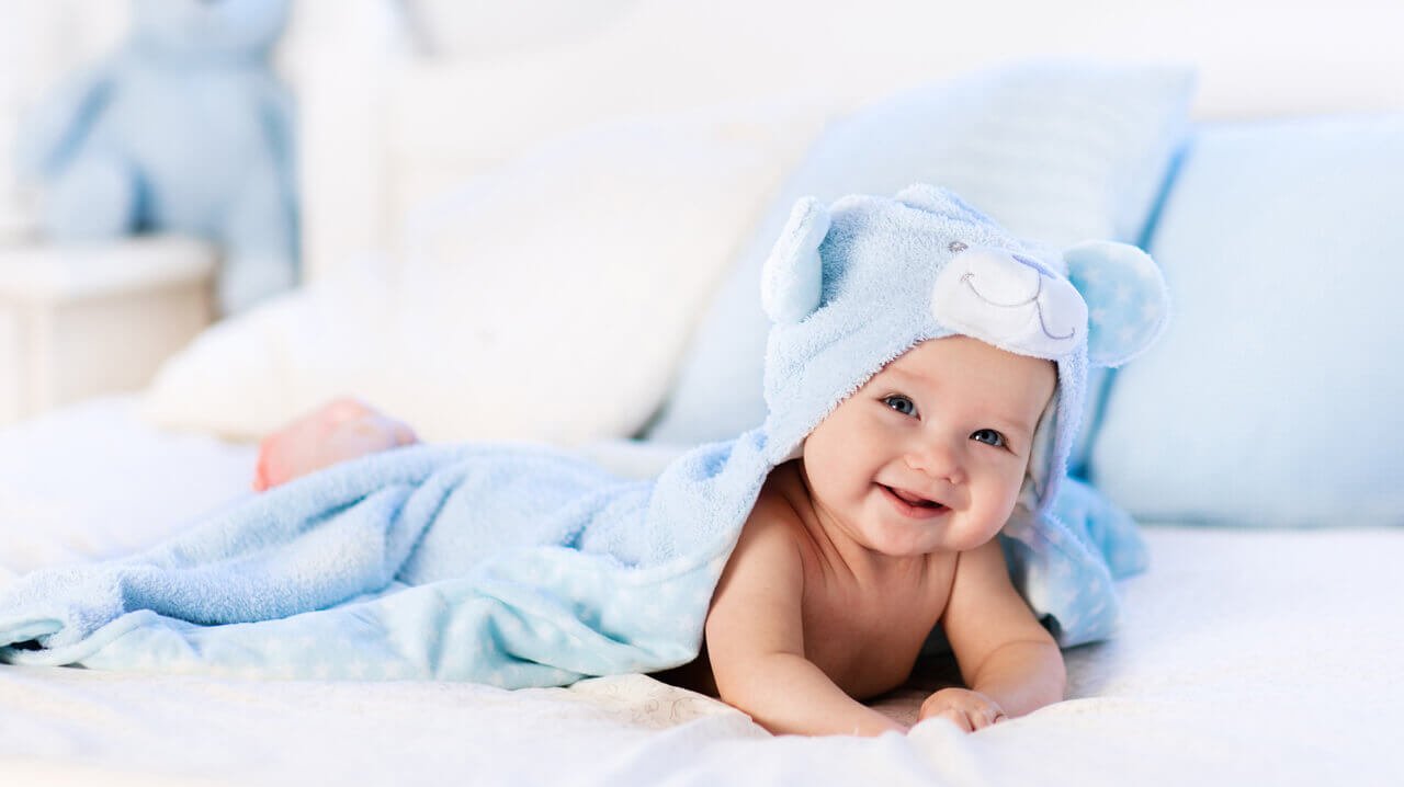 Ein Baby ist eingewickelt in einer blauen Decke mit Teddybär-Kapuze.
