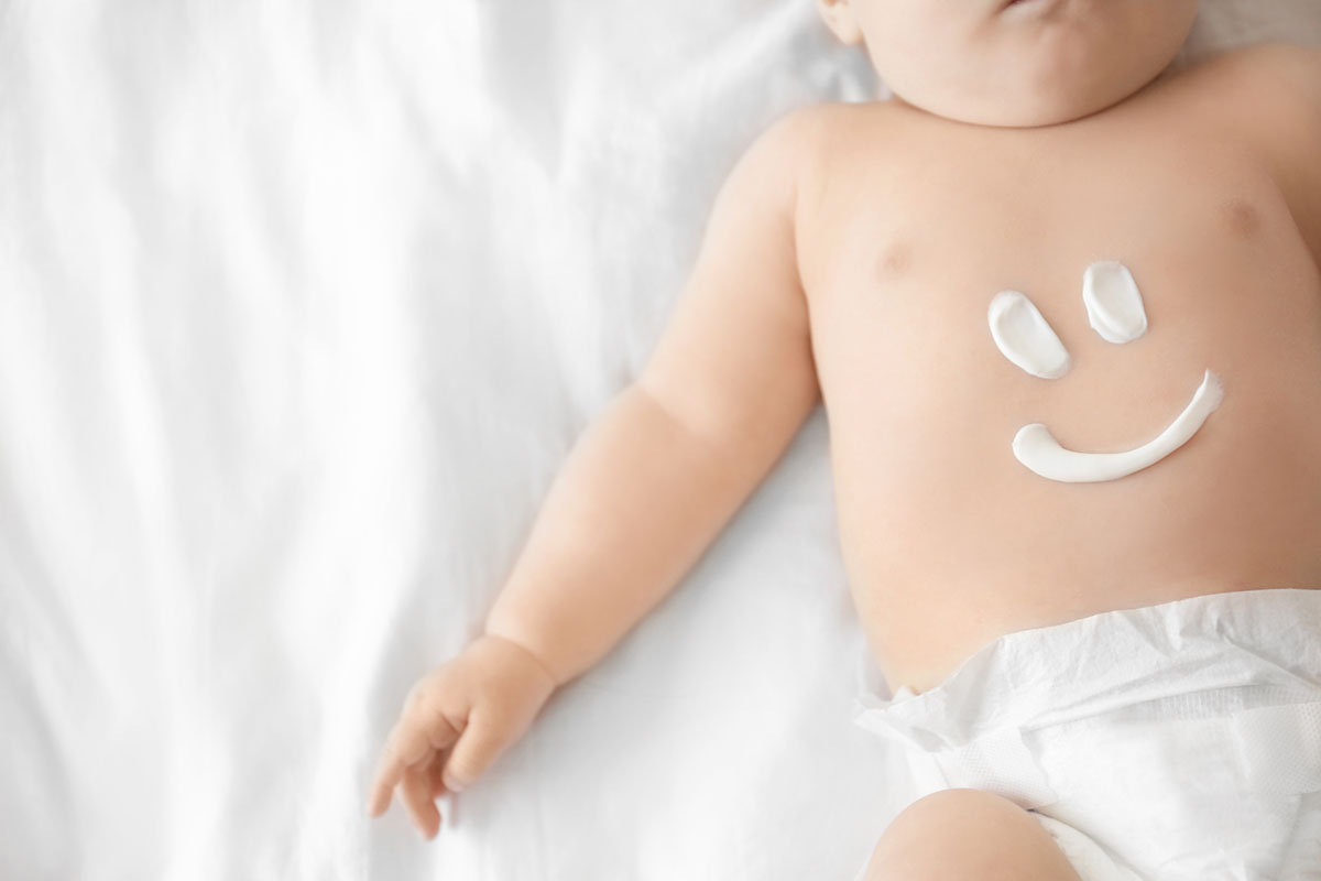 Baby mit Creme in Form eines lachenden Gesichts auf der Brust als Sinnbild für das richtige Eincremen von Babys
