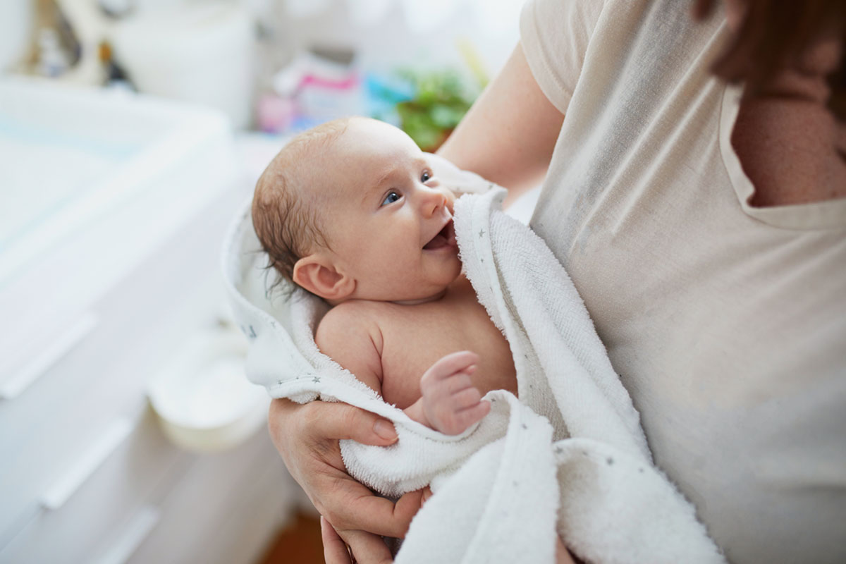 Mother lovingly holds her baby wrapped in a towel after bathing, symbolising gentle bathing for dry baby skin