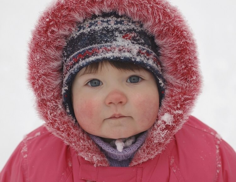 Portrait eines Kleinkindes im roten Anorak mit fellbesetzter Kapuze und Mütze bei Kälte